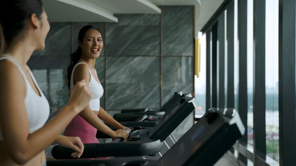 Two women smiling while walking on treadmills.